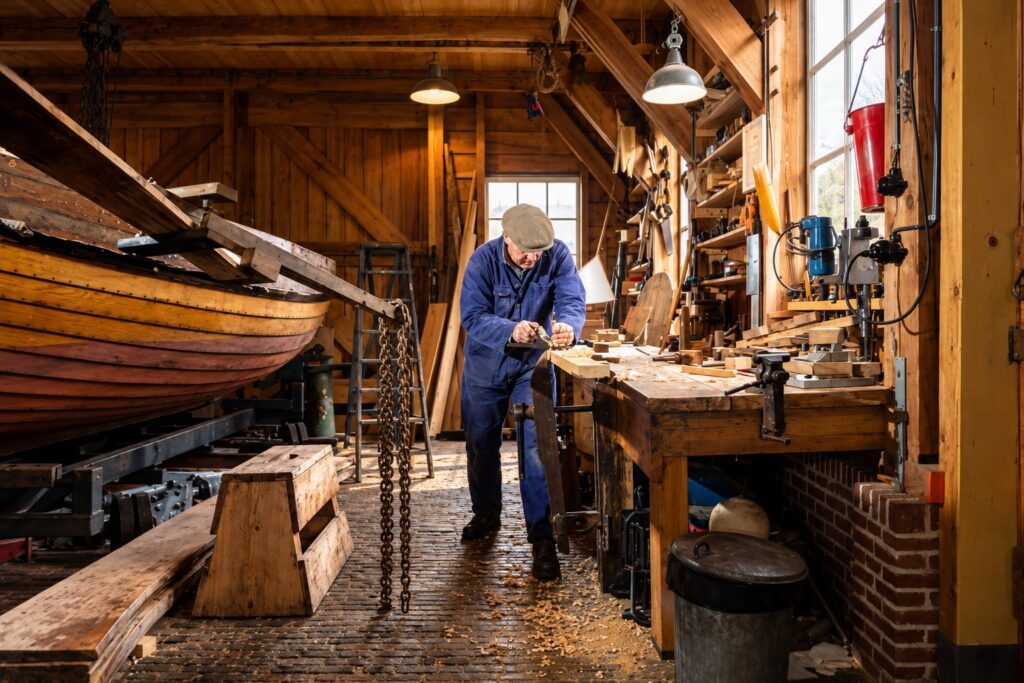 Maestro d'ascia al lavoro nel cantiere accanto a uno scafo in legno sullo scalo